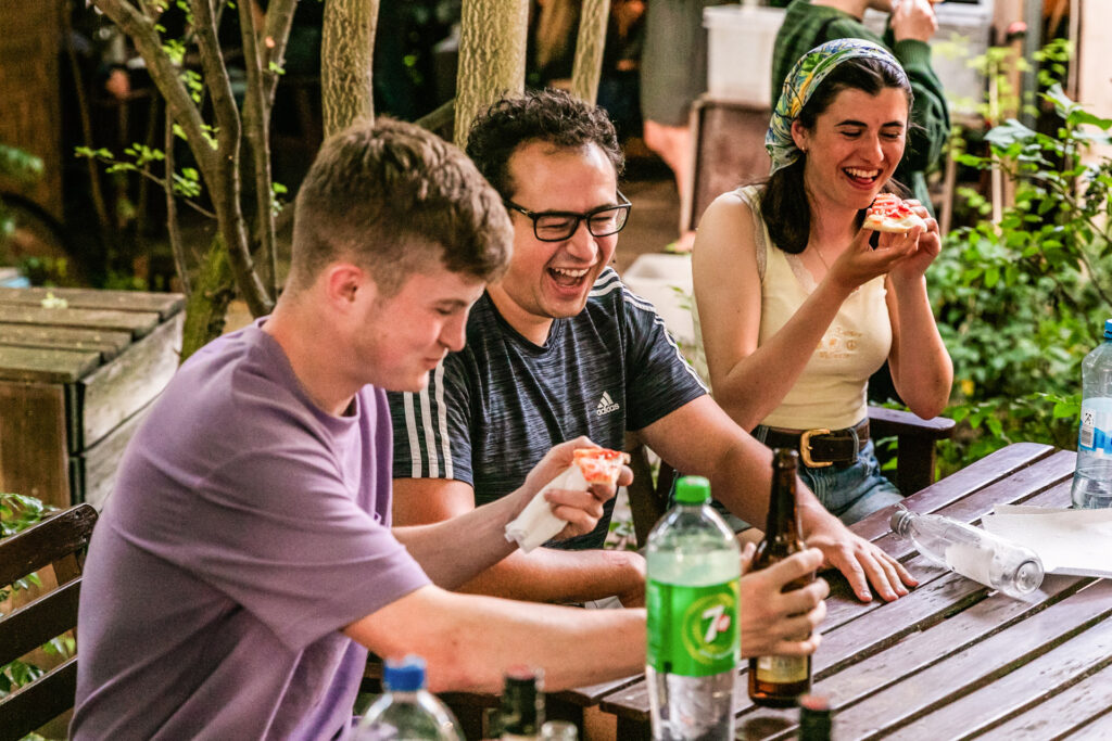 Young travellers enjoy pizza and drinks together in the outdoor area of their accommodation at EastSeven Hostel Berlin.