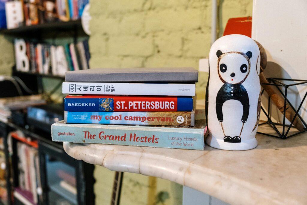 Bücherstapel mit Reiseführern und dekorativer Panda-Matrjoschka auf einem Tisch - Hostel vs. Jugendherberge