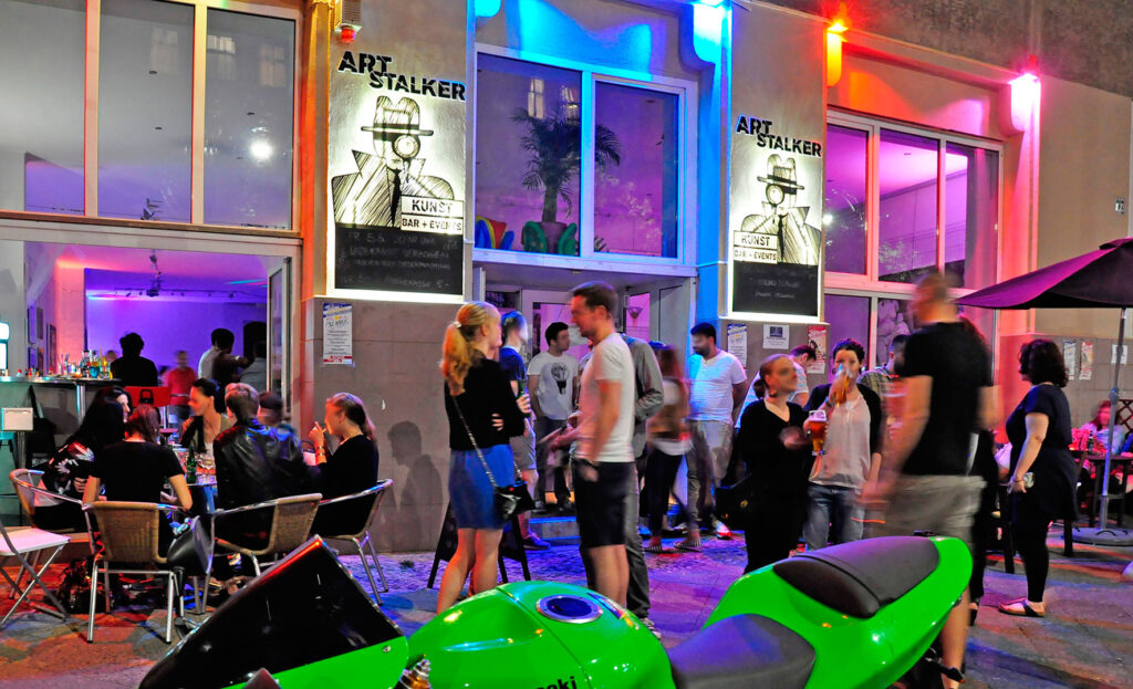 Lively bar ‘Art Stalker’ at night with colourful lights and lots of guests, ideal for extraordinary places to celebrate birthdays in Berlin.