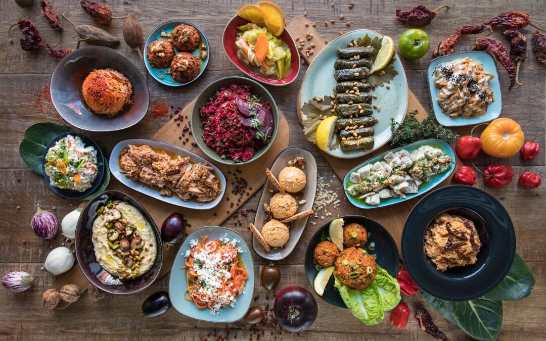 Vielfältige kulinarische Gerichte auf einem Holztablett, darunter gefüllte Weinblätter, Hummus, frische Salate, gefüllte Teigtaschen und orientalische Süßigkeiten, präsentiert als Teil der gastronomischen Erlebnisse in Berlin, besonders in Prenzlauer Berg.